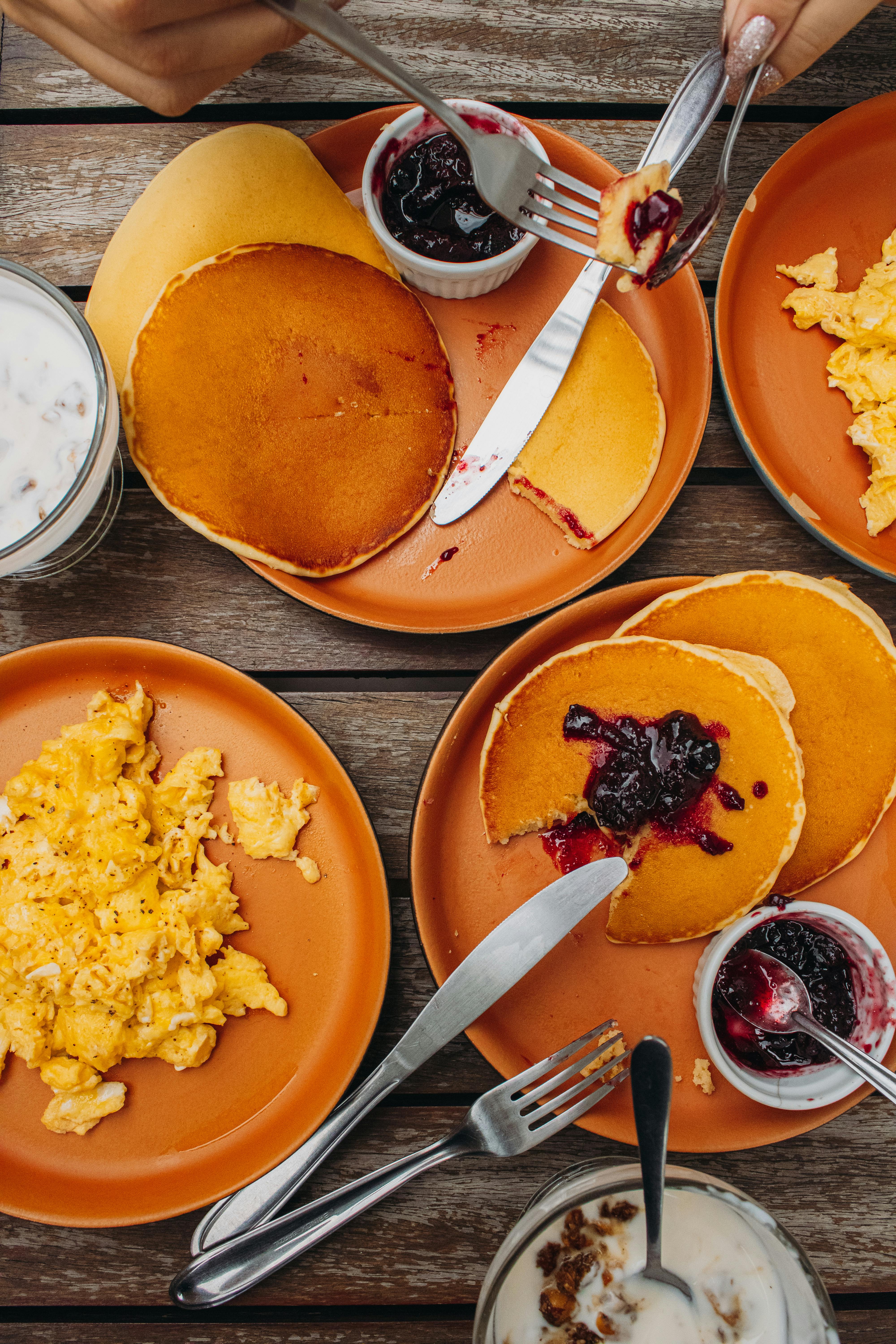 Top view of a delicious breakfast with pancakes, scrambled eggs, and jam on wooden table.
