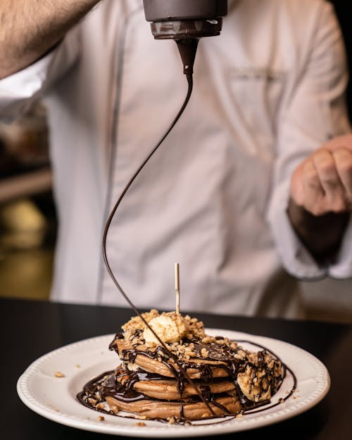 Man Squeezing Chocolate on Pile of Pancakes