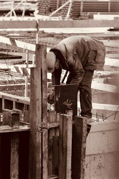 A construction worker focuses on his task at an urban building site captured in sepia tones.