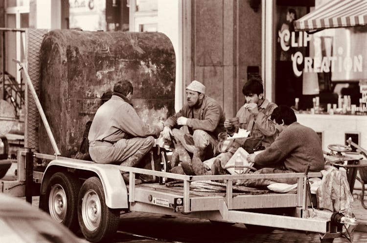 Sepia Photo Of A Group Of Workers Resting And Eating On A Trailer In The City