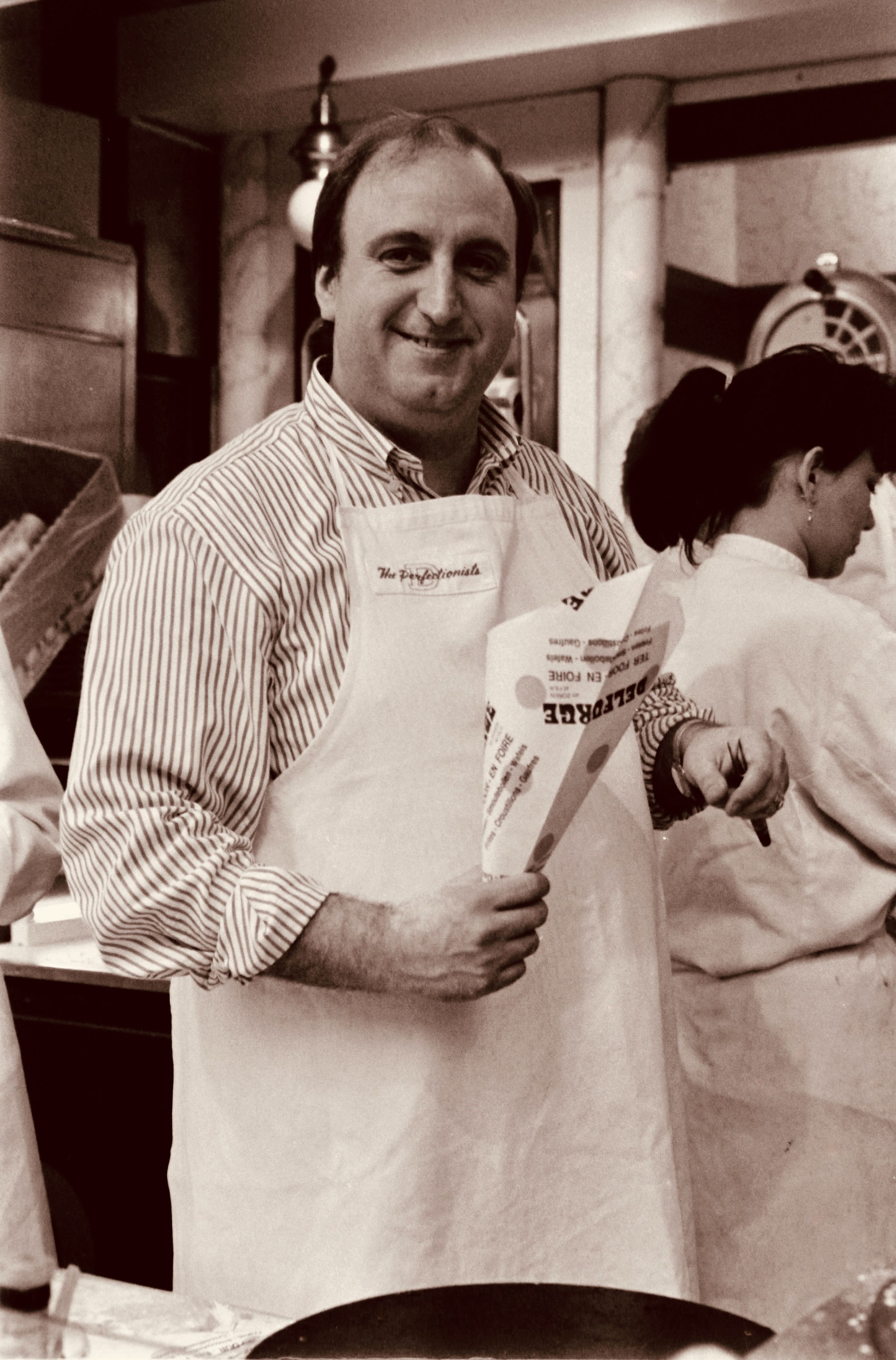 Man in apron smiling while preparing French fries at an indoor food stall.