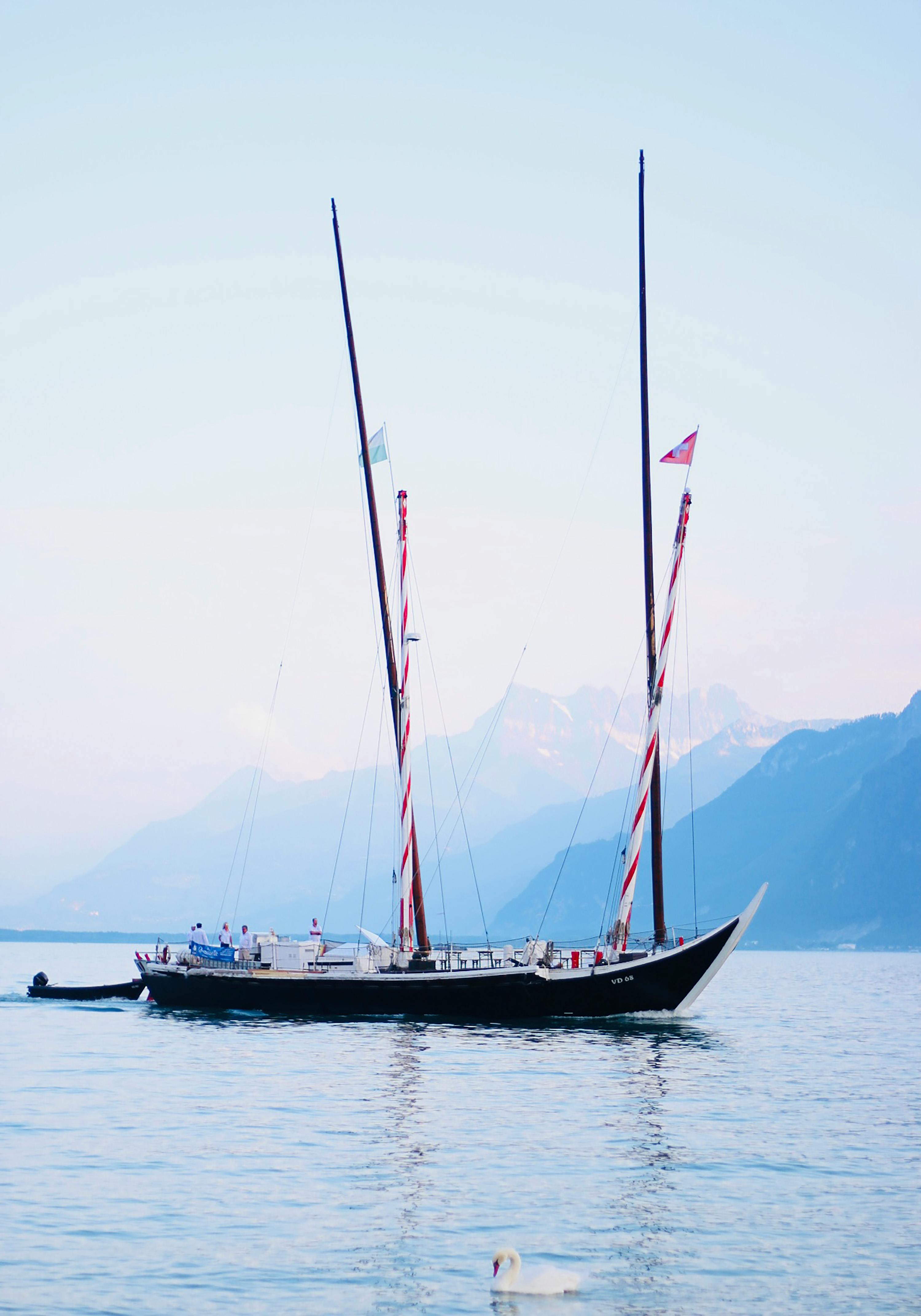 Elegant sailboat gliding on calm waters with picturesque mountains in the background.