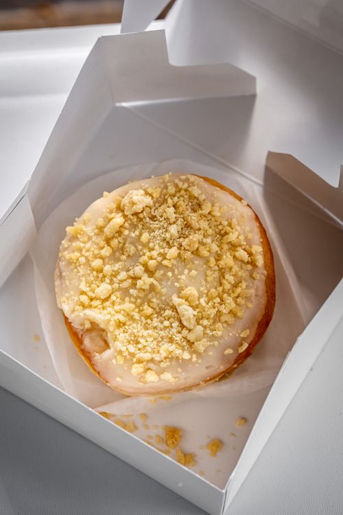 Free Delicious vanilla-glazed donut with crumb topping in a white cardboard box closeup. Stock Photo
