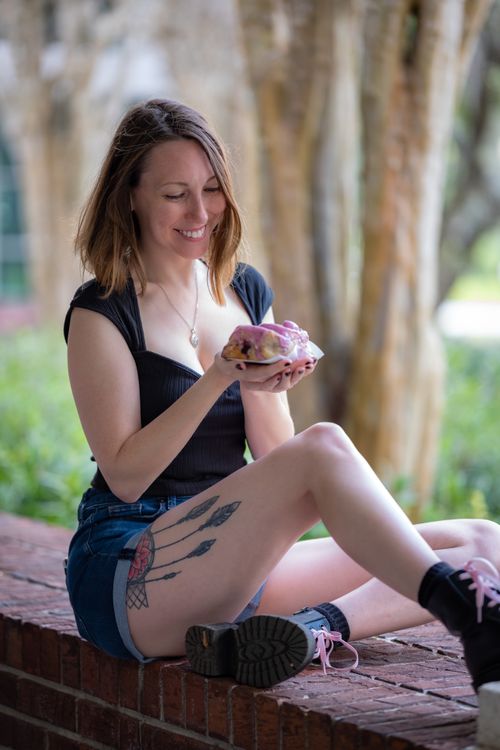 Free Woman with tattoos enjoying a donut outdoors, sitting and smiling. Stock Photo