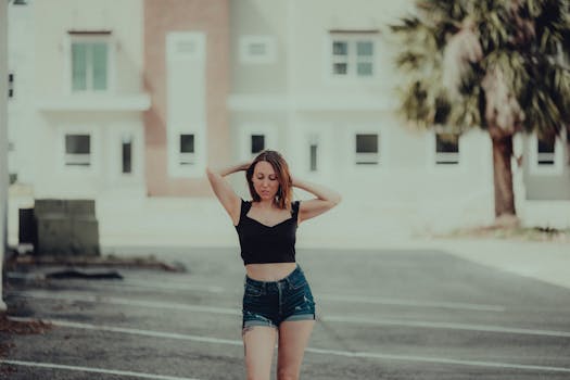 A stylish woman poses outdoors in denim shorts and black top, embodying summer fashion in an urban setting.
