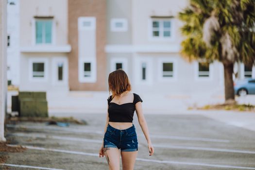 Young woman in casual summer attire walks outside in urban setting, embodying modern fashion trends.