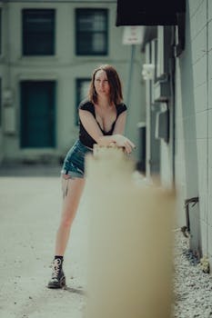 Stylish woman in shorts and boots posing in an urban alleyway, embodying edgy fashion.