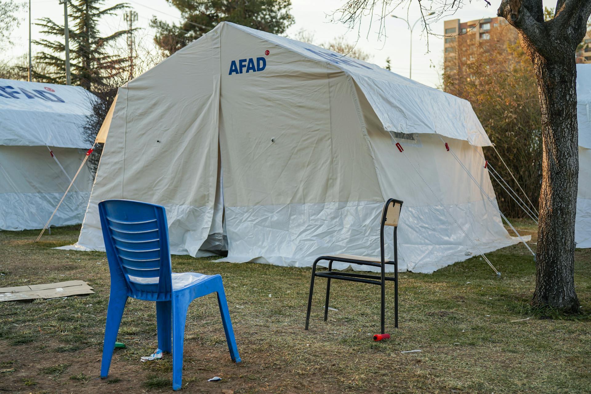 Emergency tents set up in Gaziantep for disaster relief efforts, featuring chairs and trees.