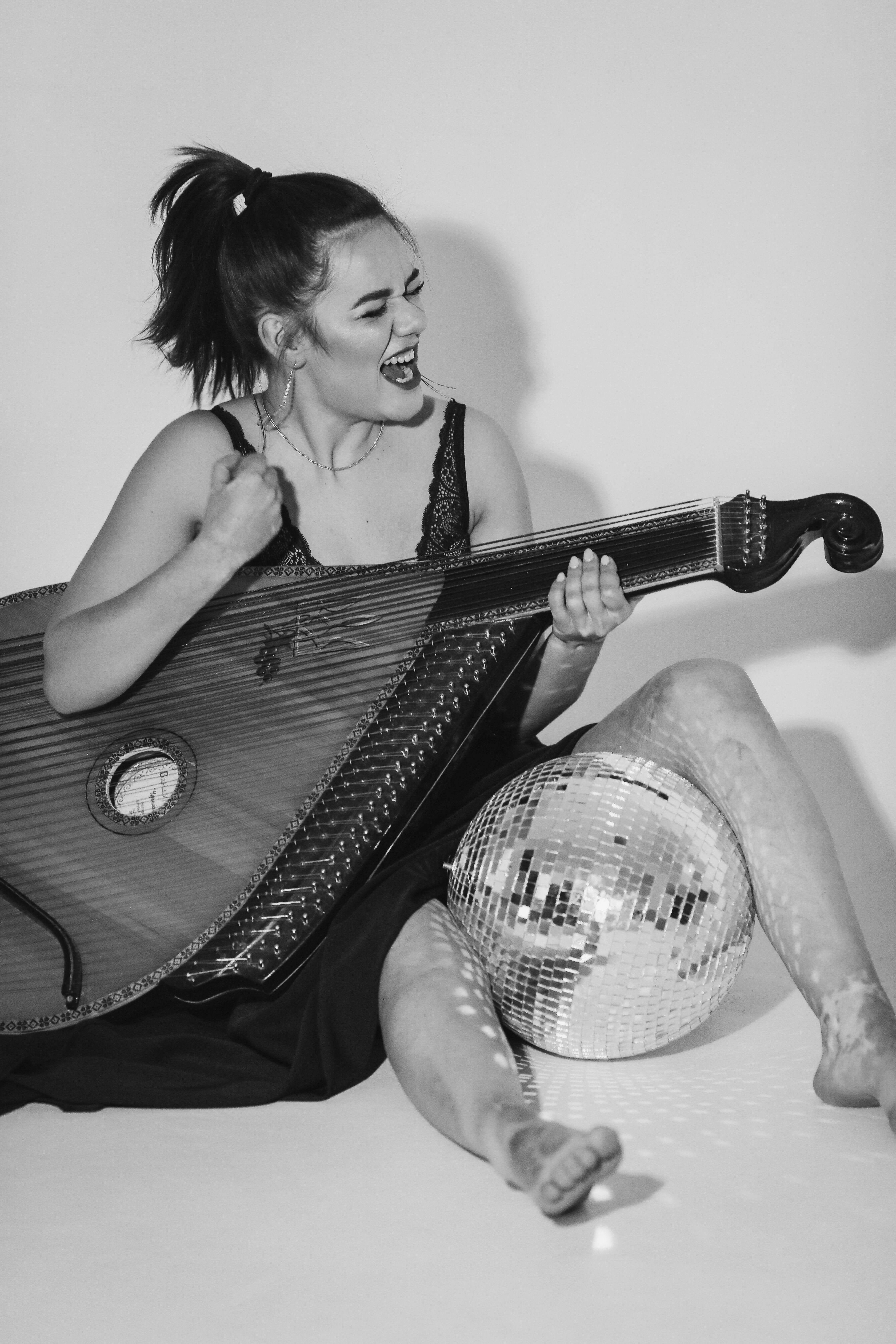 Artistic black and white photo of a woman joyfully playing a string instrument with a disco ball.