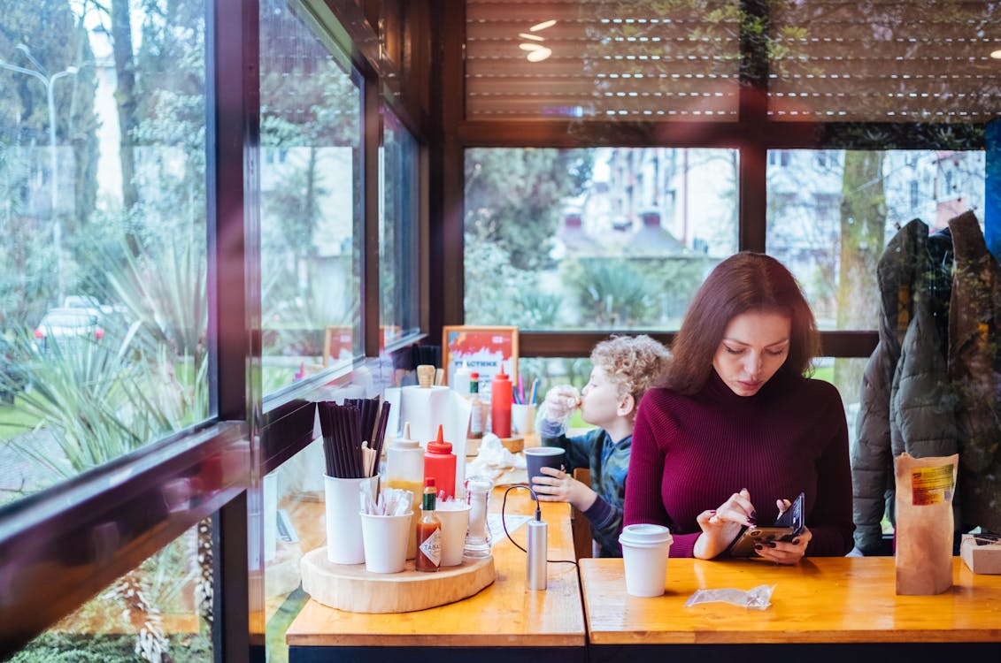 Free Woman Sitting Beside Table While Using Phone Stock Photo