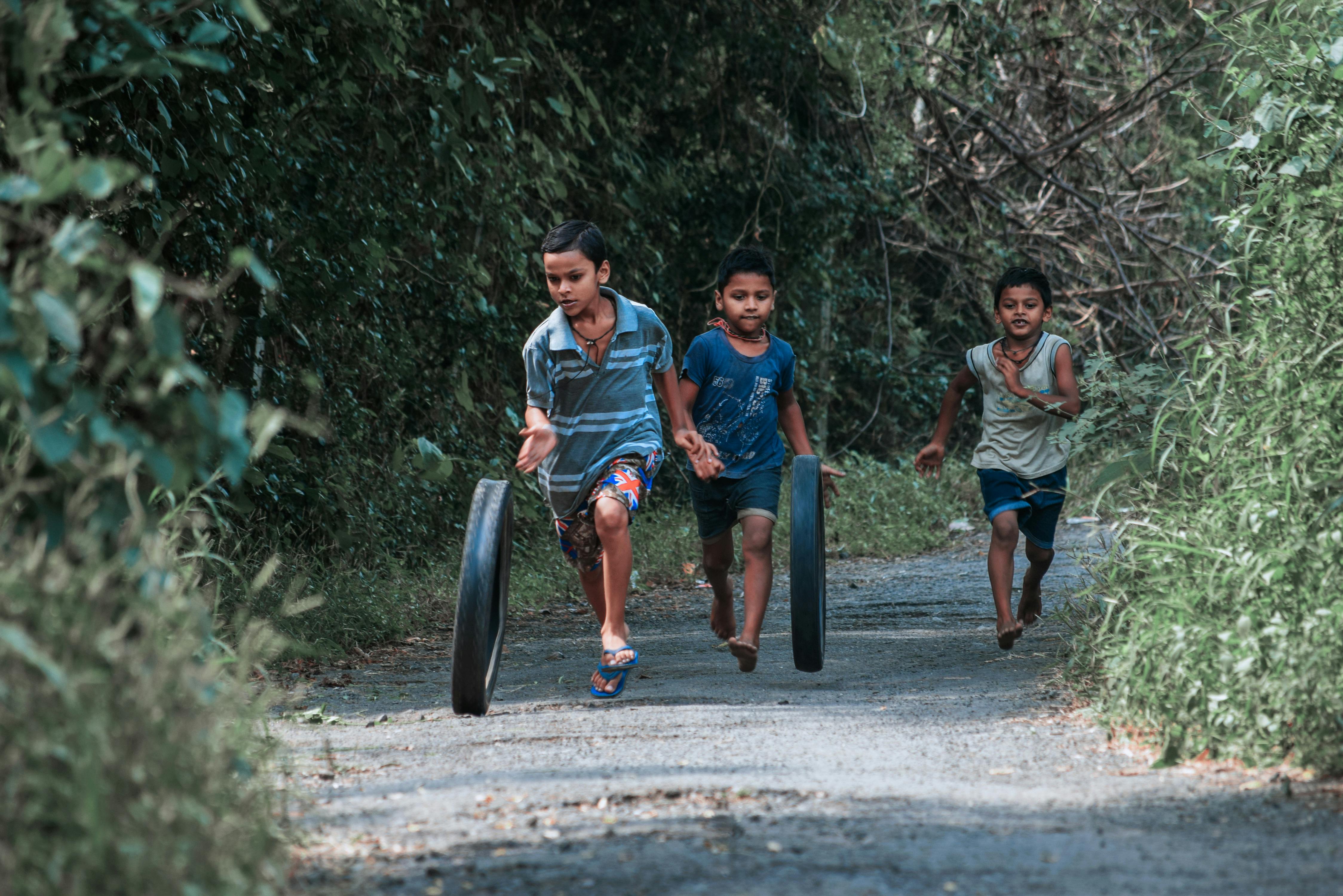 boys running and rolling tires on dirt road in forest