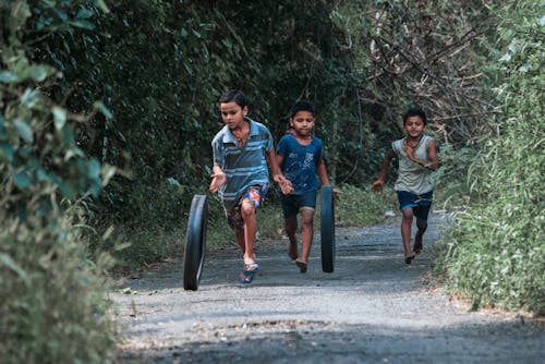 Boys Running and Rolling Tires on Dirt Road in Forest
