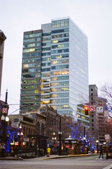 A towering modern skyscraper amidst a city street with vibrant lights at dusk.