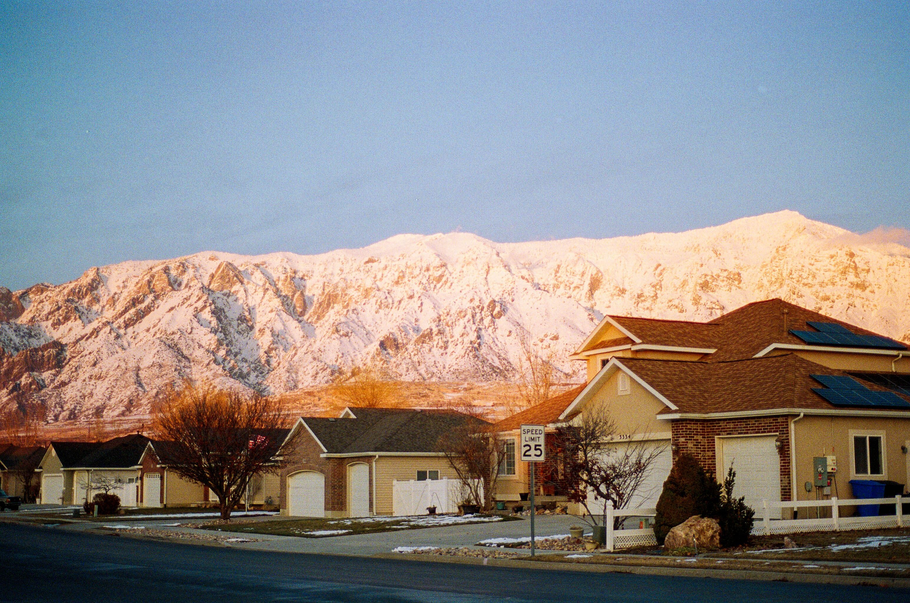 A serene winter scene with snow-capped mountains and a suburban neighborhood bathed in warm sunlight.
