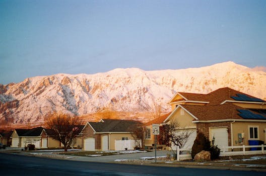 A serene winter scene with snow-capped mountains and a suburban neighborhood bathed in warm sunlight.