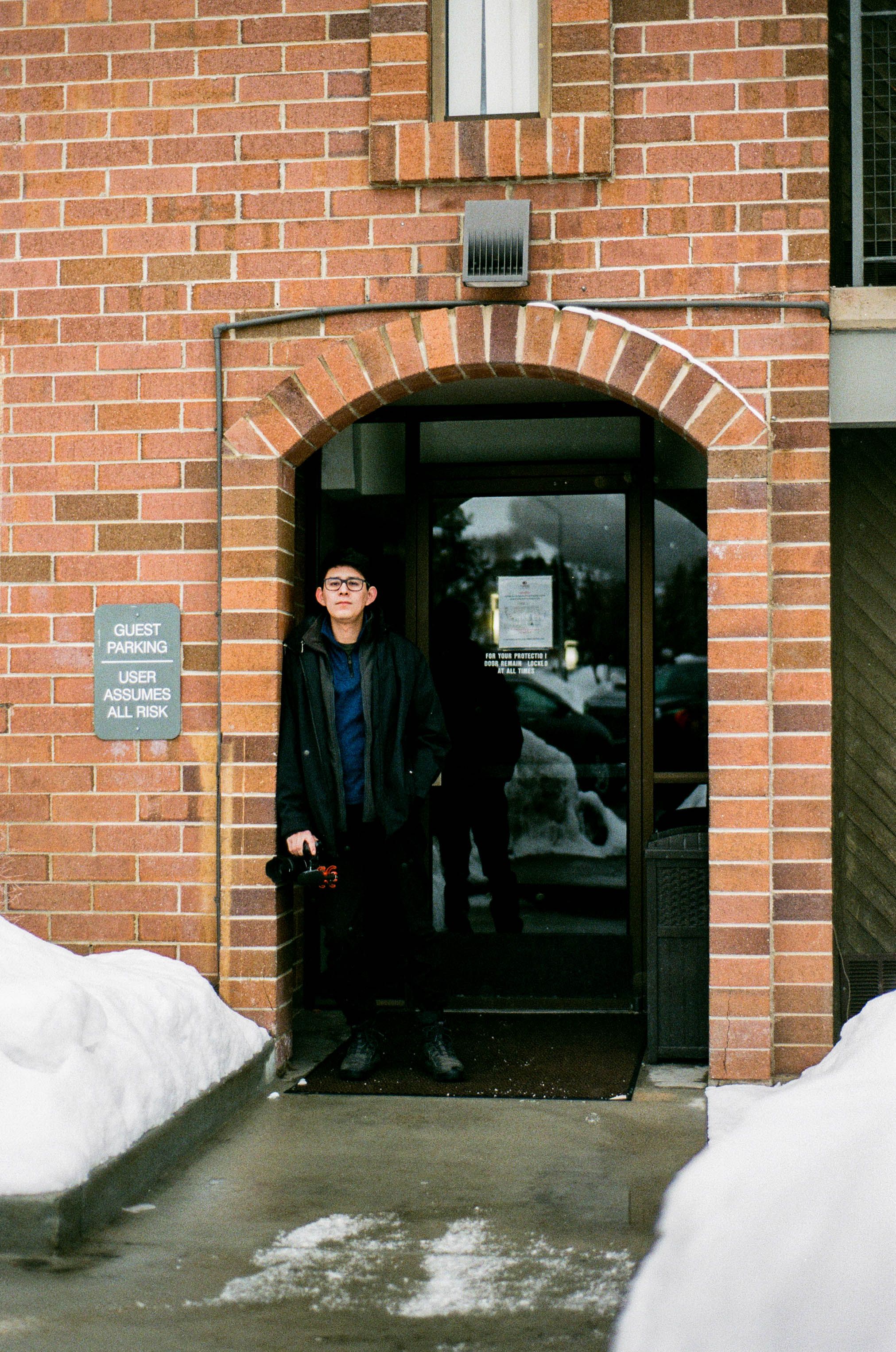 Creator in a winter coat standing in the doorway of a brick institute building — David Guerrero on Pexels