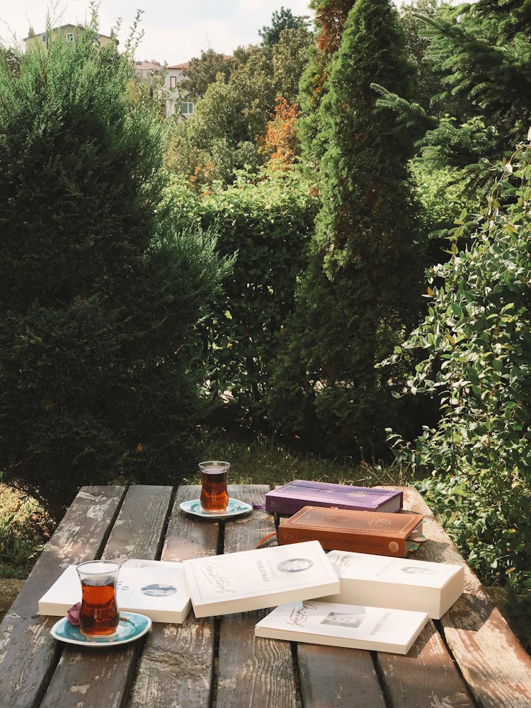 Books And Cups Of Tea On Wooden Table In Yard