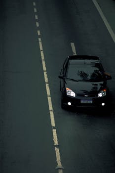 Aerial view of a black car on an empty road with a focus on its sleek design.
