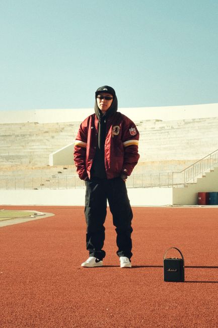 Stylish young man in casual clothing standing confidently on a red track under clear skies.