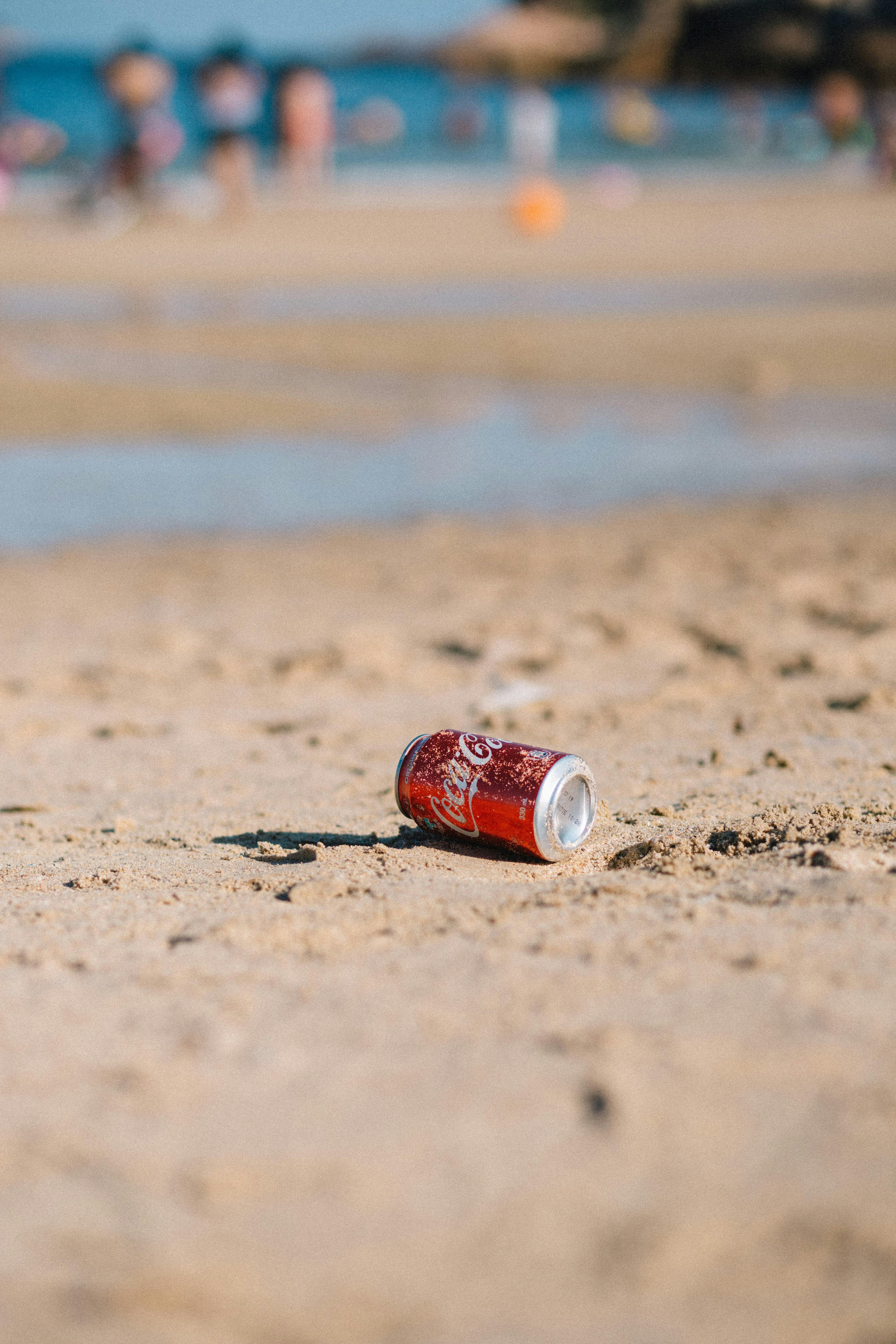 Close-up of a Coca Cola can on a sandy beach, highlighting environmental impact.