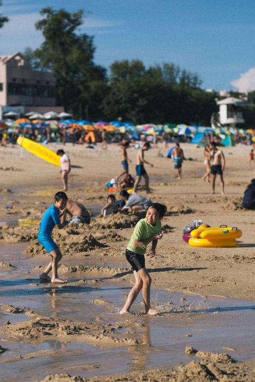 Free Kids playing joyfully on a crowded sandy beach under the summer sun. Stock Photo