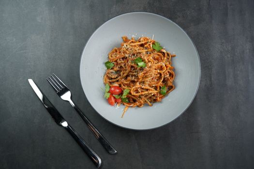 A savory plate of spaghetti served with cherry tomatoes and fresh herbs on a modern table setting.