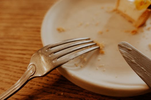 A close-up shot of a fork and knife on a plate with food remnants on a wooden table.