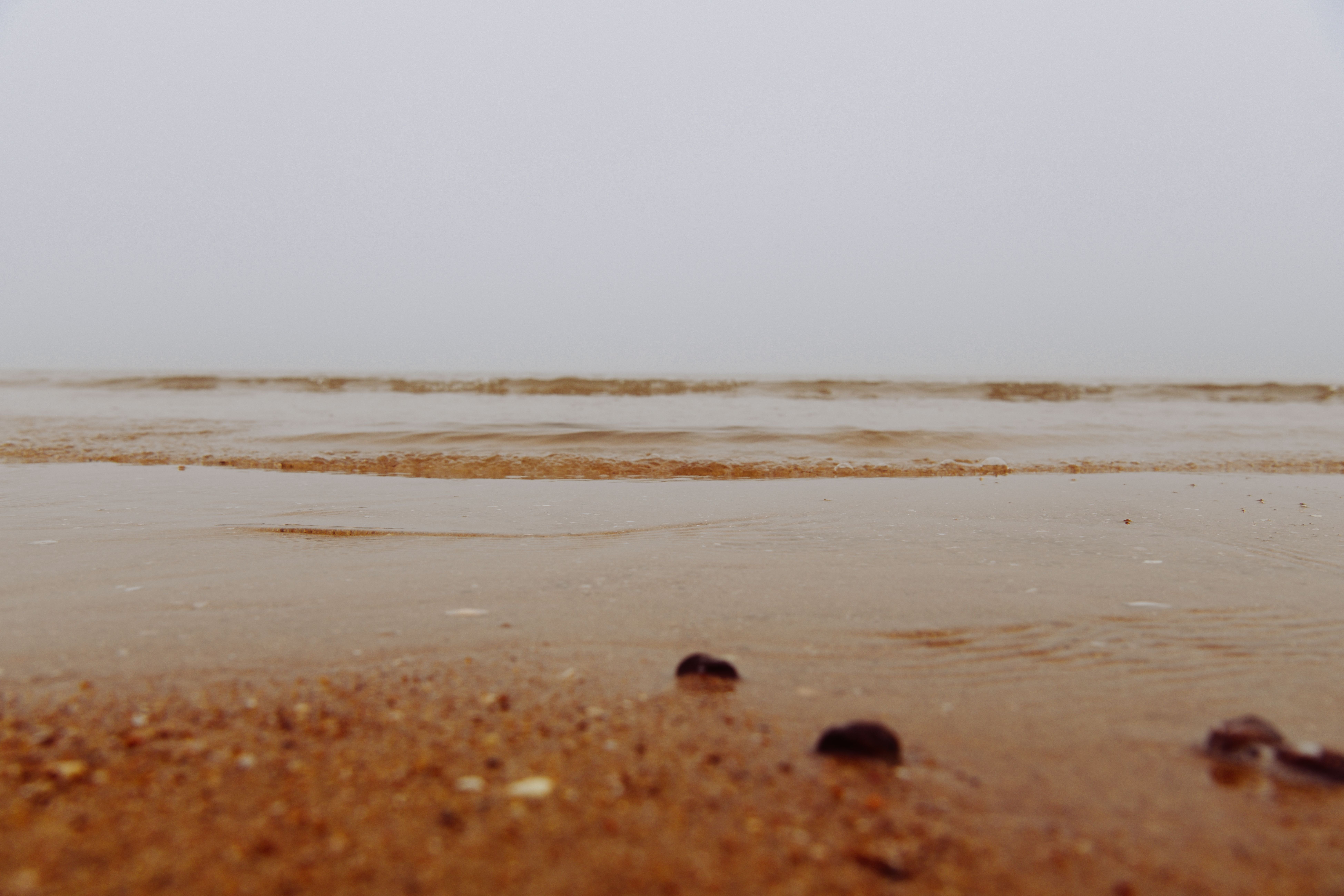 Calm ocean waves lapping onto sandy shore on an overcast day, creating a tranquil coastal scene.