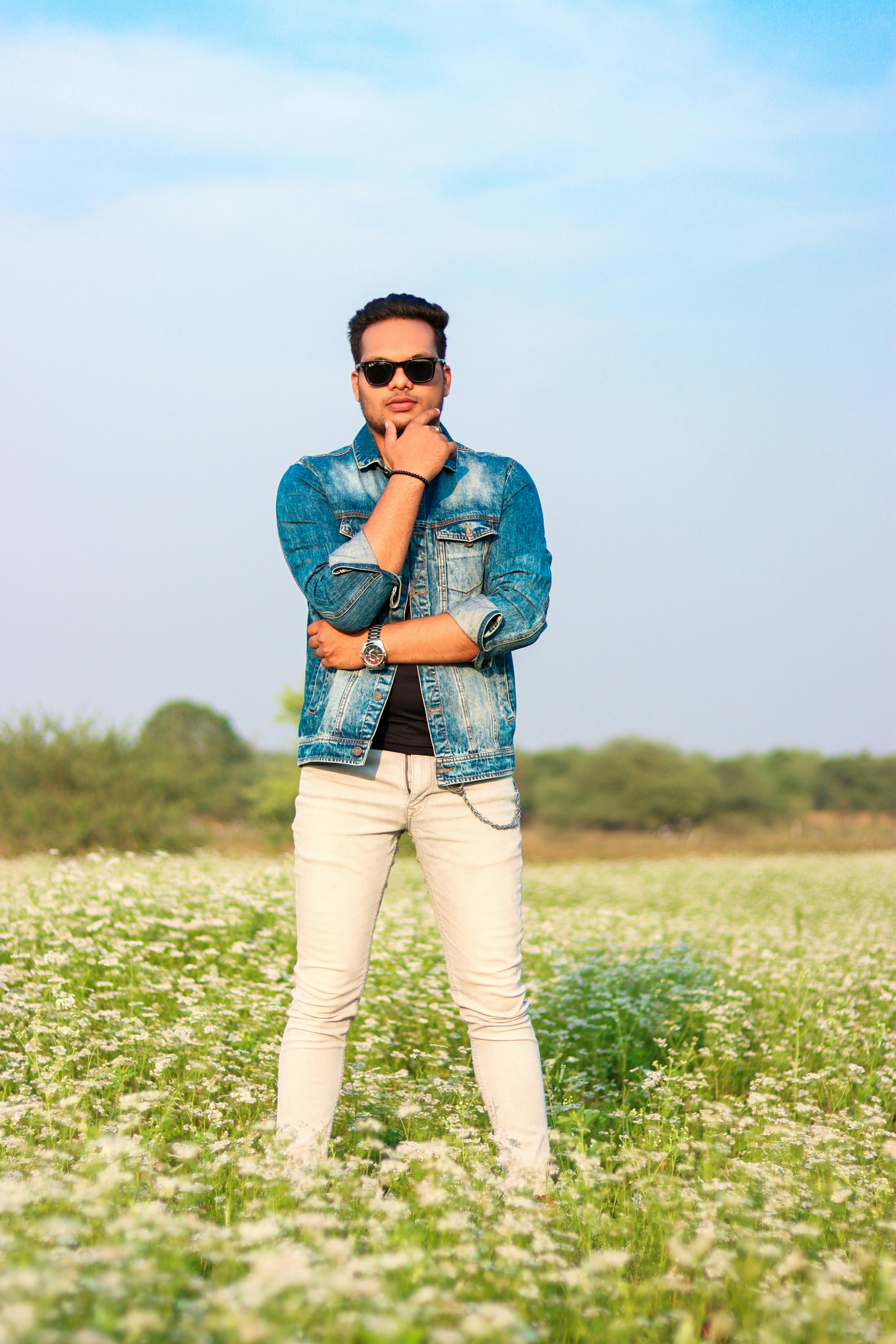 A trendy young man posing in a field of white flowers on a sunny day.