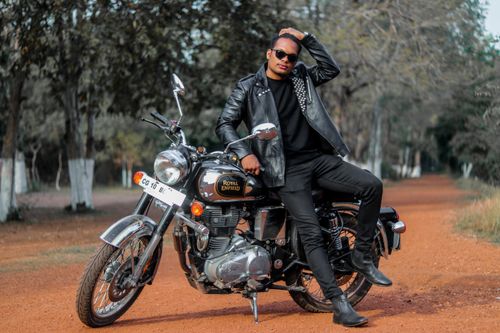Free A stylish young man poses with a Royal Enfield motorcycle on a dirt road, showcasing fashion and adventure. Stock Photo