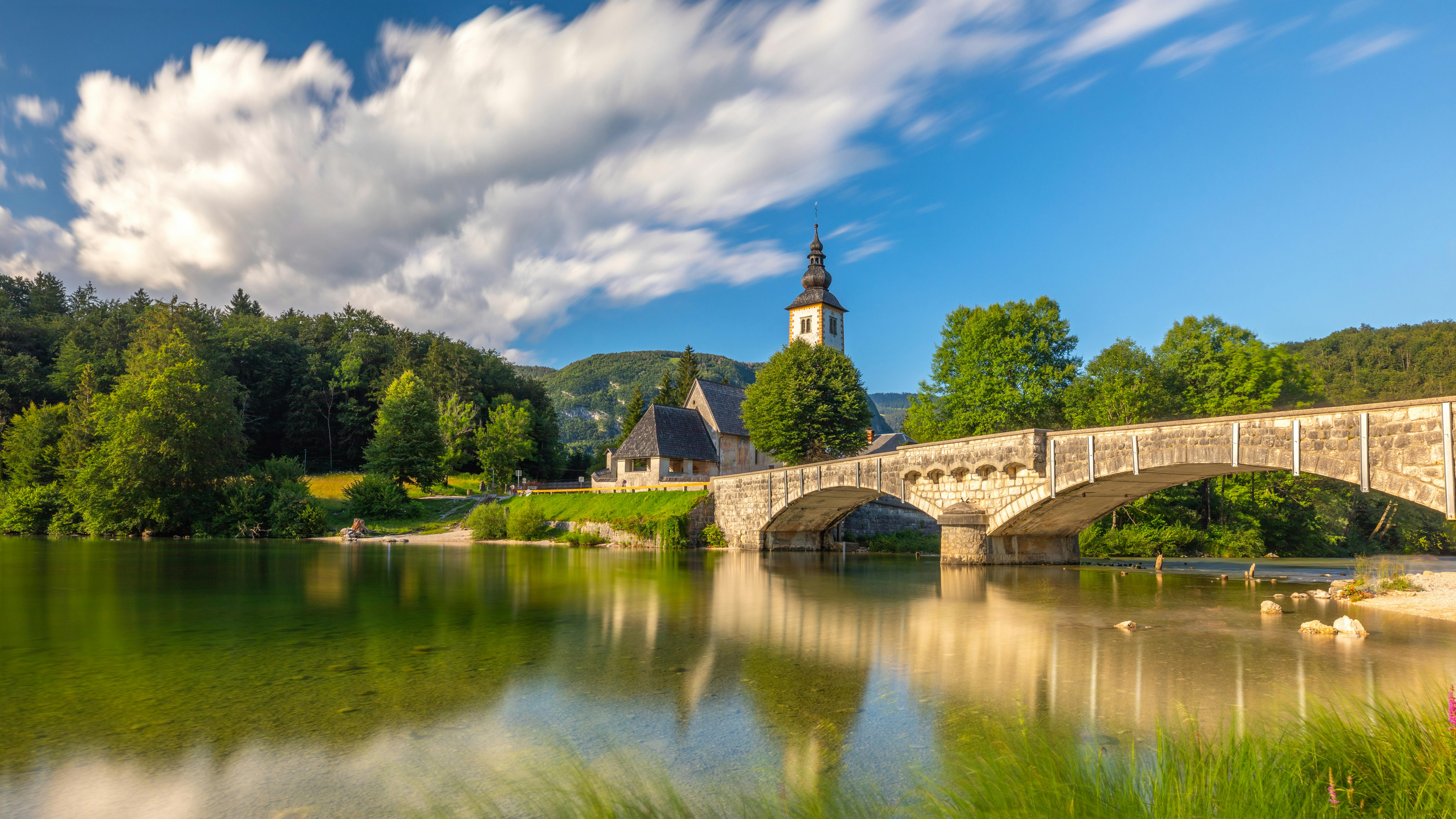 long exposure sunny nature landscape with mountain lake in slovenia beautiful lake bohinj with perfect sky at summer view on calm lake with azure water church and stone bridge on backgr