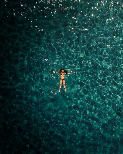 Free Drone shot of a woman floating in clear blue waters of La Maddalena, Italy Stock Photo
