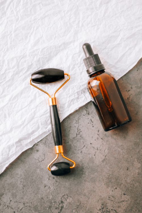 Free Elegant flat lay of a jade face roller and essential oil bottle on a textured surface for spa treatments. Stock Photo