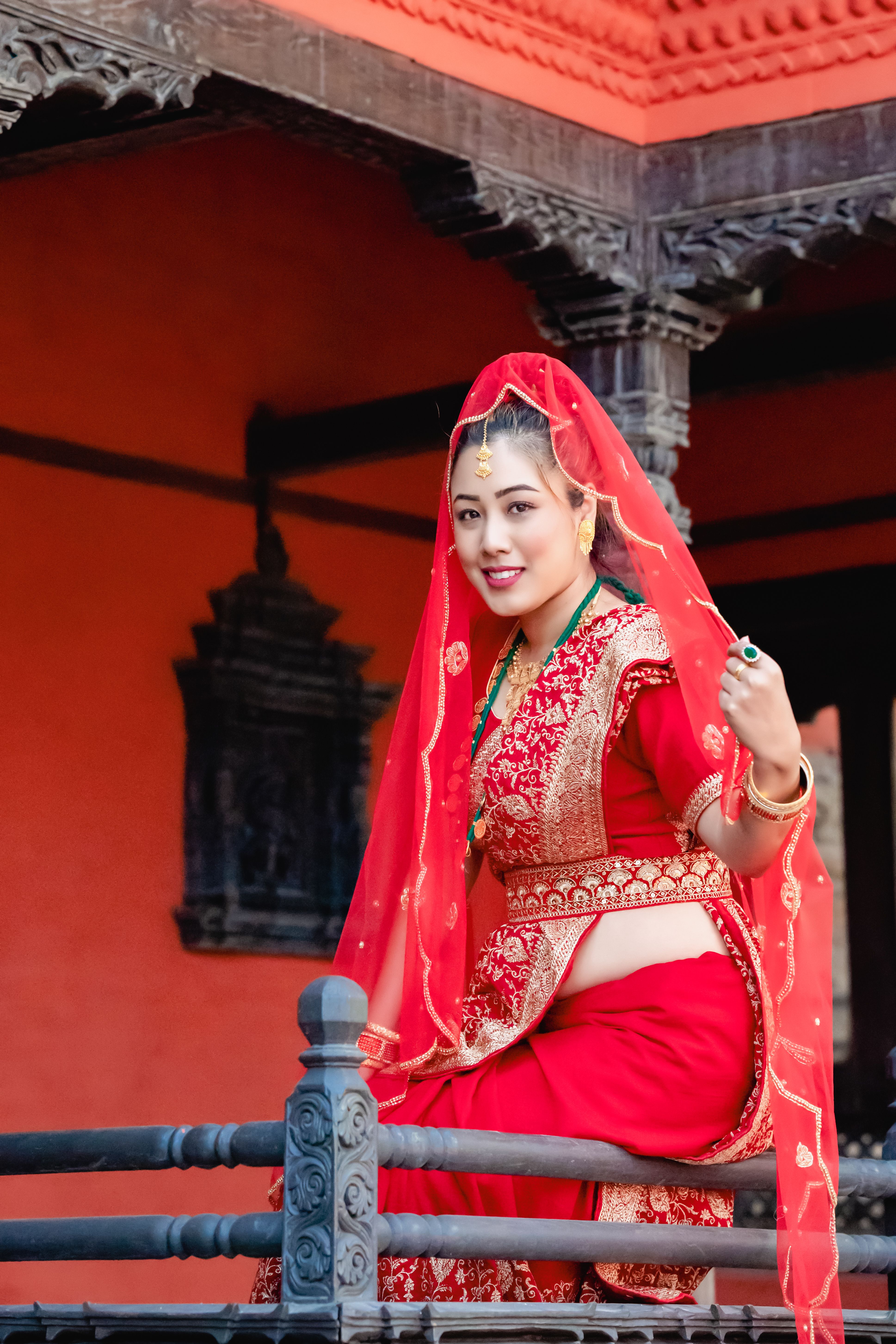Elegant bride in vibrant red traditional dress sitting gracefully on a railing.