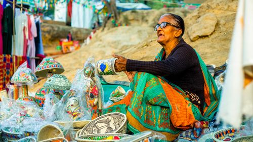Free Elderly woman selling colorful traditional handicrafts at an outdoor market. Stock Photo