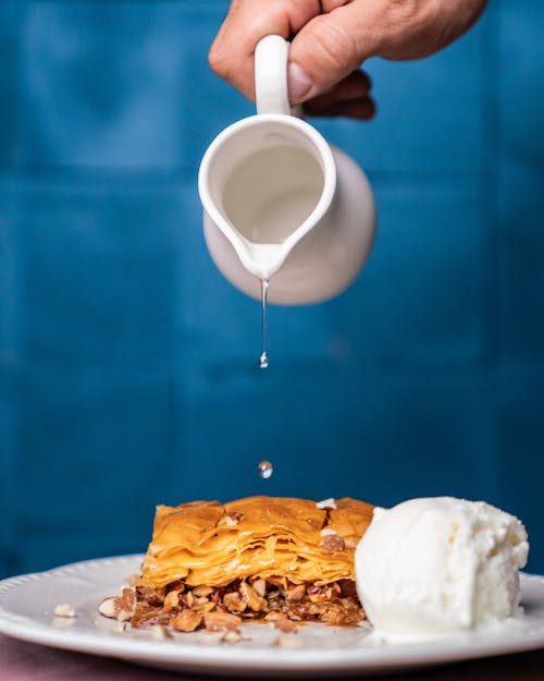 Close-up of a Person Pouring Liquid on a Slice of Baklava with a Scoop of Ice Cream 