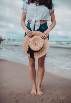 Fashionable woman holding straw hat on Międzyzdroje beach in Poland during summer.