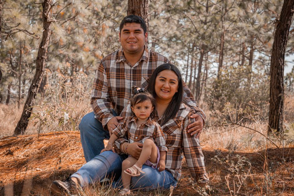 Una familia alegre sentada junta en un bosque, todos vestidos con camisas de cuadros a juego.