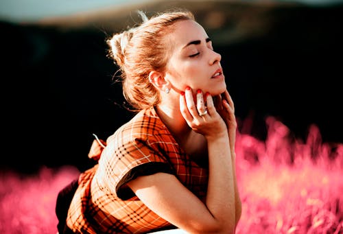 Young Woman in a Plaid Orange Blouse Posing in a Pink Meadow