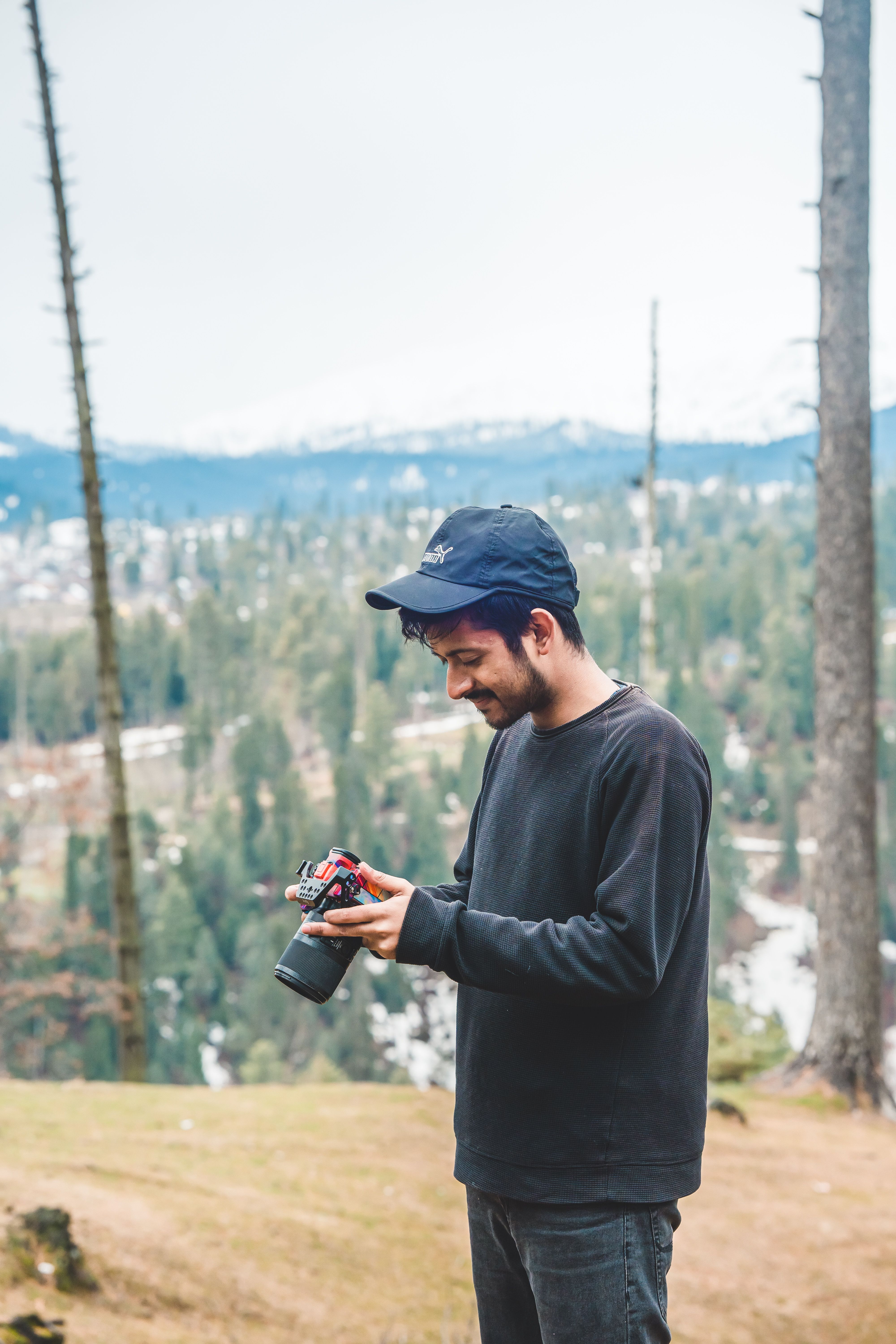Smiling man in a cap holding a camera in a serene forest setting, embracing nature.