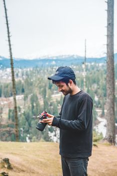 Smiling man in a cap holding a camera in a serene forest setting, embracing nature.