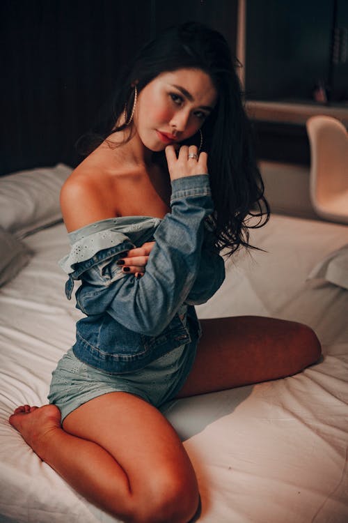 Young Woman in a Denim Jacket and Blue Mini Dress Sitting on the Bed