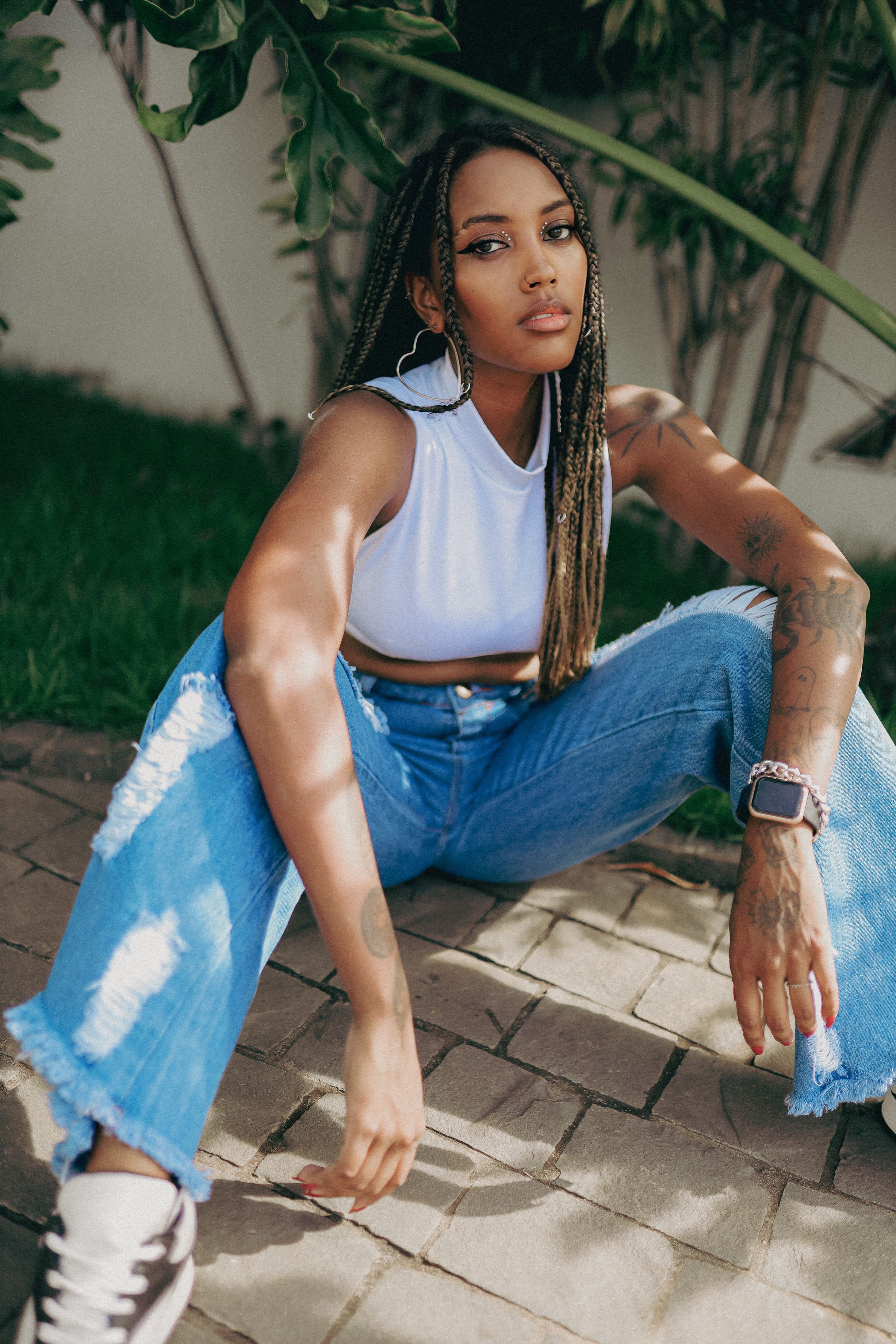 Portrait of an African American woman in casual attire with braids sitting on pavement outdoors.