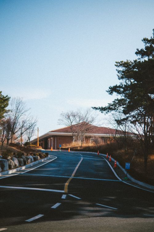 Free A peaceful urban road curves towards a rustic building under a clear blue sky with bare trees. Stock Photo