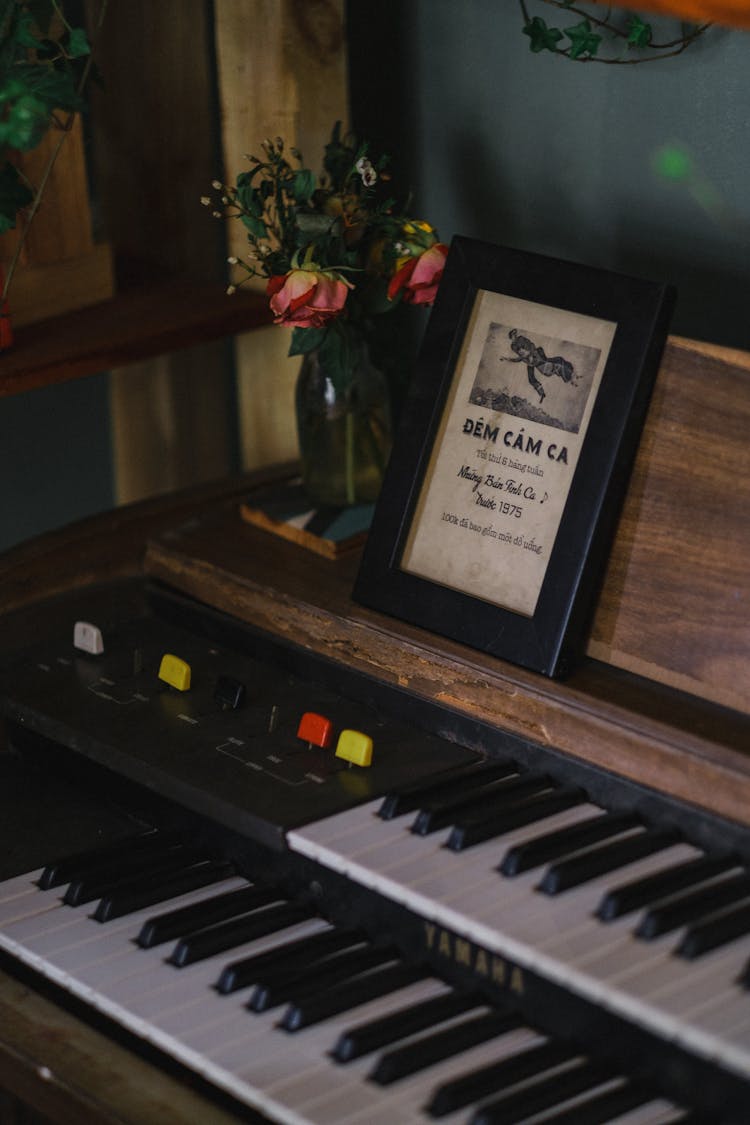 A Framed Picture And Flowers On A Piano 