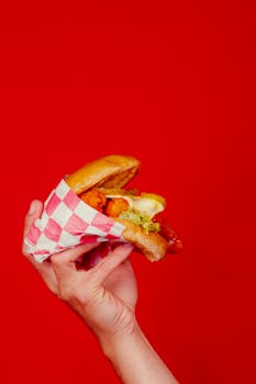 Vibrant close-up of a delicious burger held with a red background, perfect for food marketing.