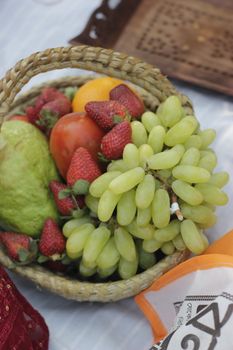 Colorful basket of mixed fruits including strawberries and grapes on a table.