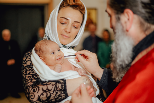 Free A smiling baby during a baptism ceremony, held by a mother wearing a headscarf. Stock Photo