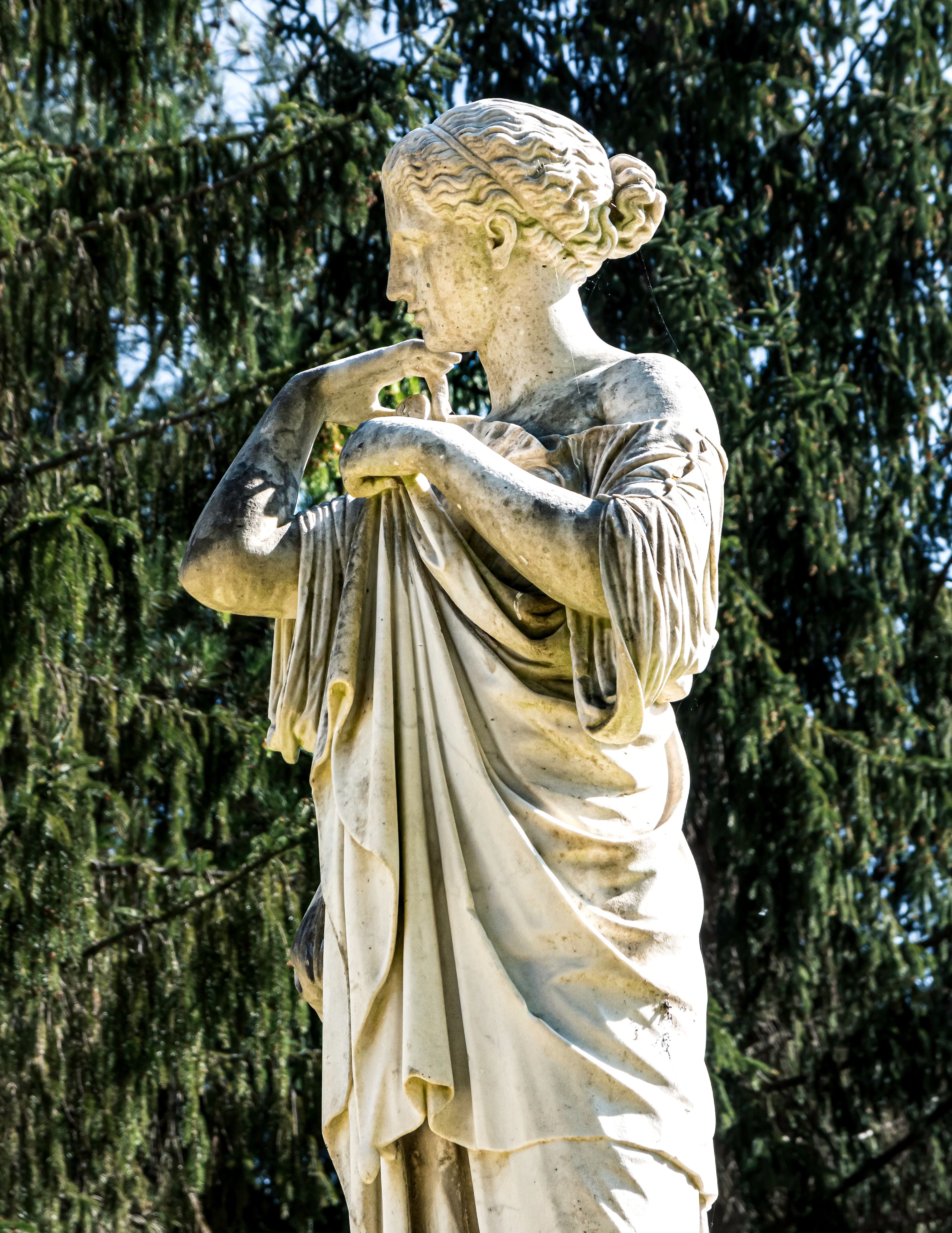 A classic statue of a woman elegantly posed in an outdoor park, surrounded by lush greenery.