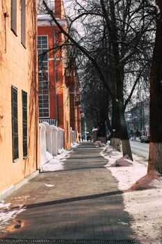 Scenic winter urban sidewalk with snow and sunlight creating intricate shadows of trees.